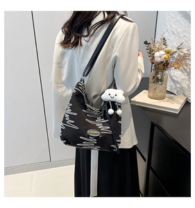 Detail of black canvas tote with wave embroidery and white cloud pendant shown on shoulder