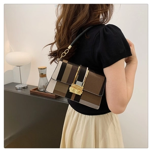 Detail of color-block shoulder bag with gold metal clasp worn by a female model