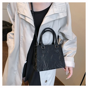 Detail of black pleated PU leather handbag featuring polished gold hardware and crossbody strap