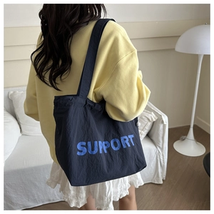 Detail of navy canvas tote bag with SUPPORT print worn on shoulder in home setting