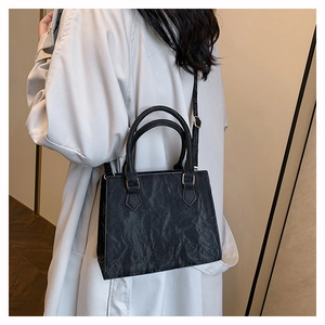 Detail of minimalist black tote bag with vintage crinkled texture and gold hardware
