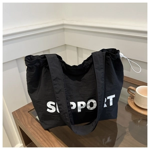 Detailed view of black textured tote bag with Support print on a glass table