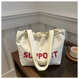 Detail of cream canvas tote bag with red SUPPORT print on dark wood tabletop