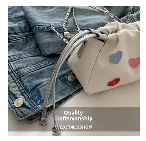 Detail of white canvas bucket bag with colorful heart patches and silver chain strap