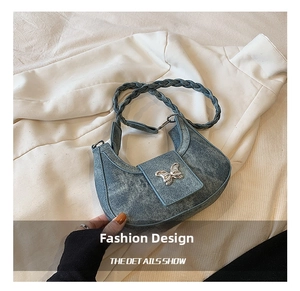 Gros plan du sac hobo en denim bleu avec boucle papillon argentée et bandoulière tressée