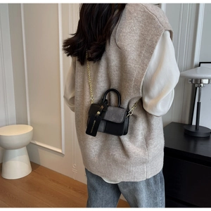 Detail of a mini crossbody bag with black and grey color-blocking and gold chain strap