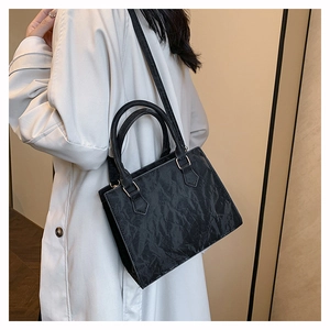 Detail of black faux leather crossbody bag with pleated texture and gold hardware