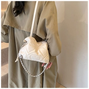 Model wearing a cream quilted heart-shaped shoulder bag with chain strap and ruched detail