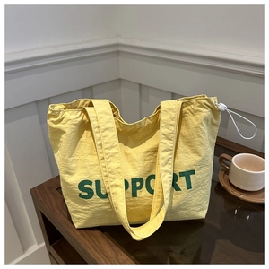 Detail view of yellow tote bag with green Support text and side drawstring buckle