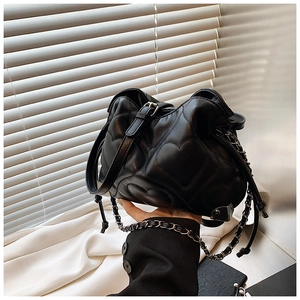 Detail of black quilted shoulder bag featuring heart pattern stitching and chain strap
