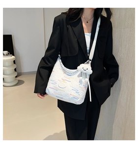 Detail of white canvas crossbody bag featuring colorful embroidery and plush cloud charm