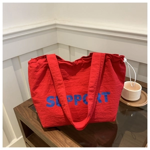 Detail of red nylon tote bag with blue Support text and white drawstring closure