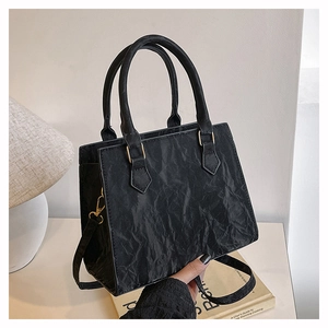 Macro detail of black pleated leather texture and gold hardware on square handbag