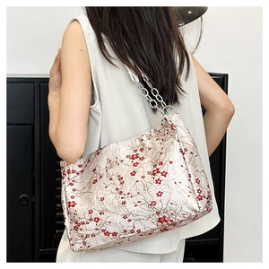 Detail of embroidered plum blossoms on a beige tote bag with a silver chain strap