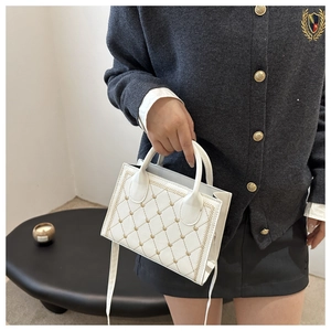 Close-up of white crossbody bag with gold heart embroidery and dual top handles