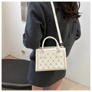 Close-up of a white quilted crossbody bag with gold heart studs and top handle