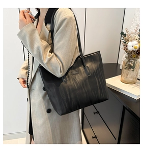 Detail of black tote bag featuring textured embossing and a metallic brand logo plate