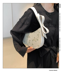 Detailed embroidery of green floral patterns on a cream lace half-moon shoulder bag