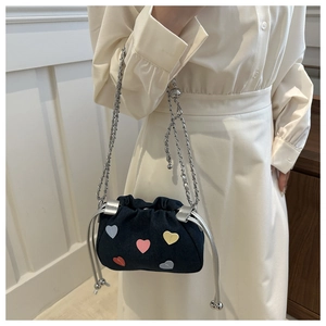 Détail d'un sac seau en denim bleu avec patchs coeurs colorés et bandoulière chaîne