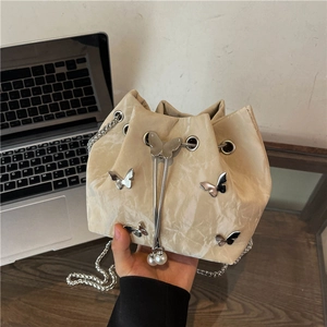 Chic cream drawstring bucket bag with silver butterfly accents and pearl chain strap