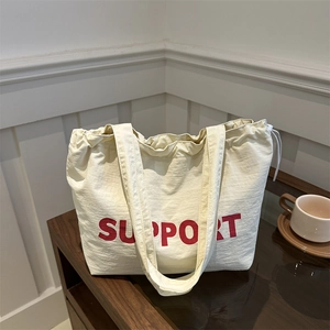Cream canvas tote bag with red SUPPORT lettering on a rustic dark wood surface