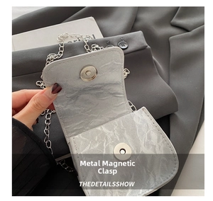 Close-up of the silver magnetic snap closure on a grey textured saddle bag with chain