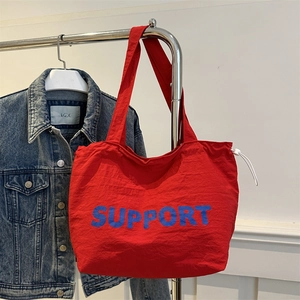 Minimalist red tote bag with Support print and wide shoulder strap hanging on rack