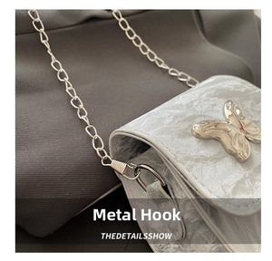 Detail of silver butterfly buckle and metallic chain on textured leather bag