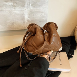 Brown quilted tote bag with heart stitching and chain strap on a lifestyle background
