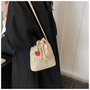 Dettaglio borsa a secchiello beige con toppe a cuore colorate su cappotto nero