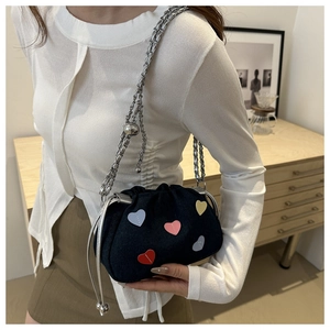 Detail of blue denim crossbody bag with colorful heart patches and silver chain strap
