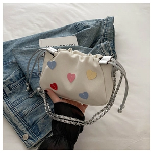 Detail of cream canvas crossbody bag with colorful heart patches and chain strap