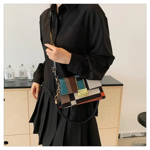 Detail of color-block crossbody bag with gold lock buckle on model in home setting