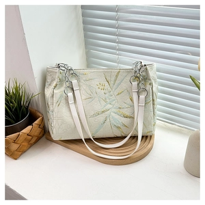 Detail of bamboo embroidery on beige tote bag with silver chain strap on wooden tray