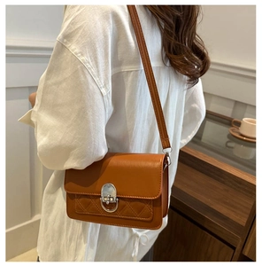 Detail van een bruine gewatteerde crossbodytas met zilveren draaisluiting en glad leer