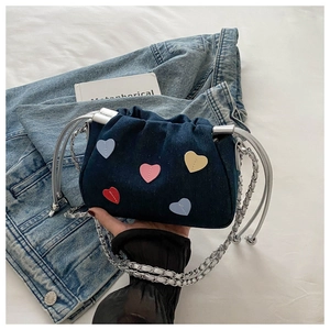 Detail of blue denim drawstring bag with colorful heart patches and silver chain strap