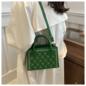 Detailed view of green quilted handbag with heart embroidery on beige trench coat