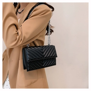 Détail d'un sac bandoulière noir matelassé avec chaîne argentée sur un mannequin en tailleur