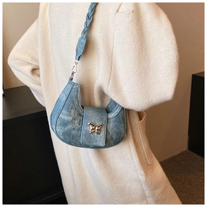 Détail du sac croissant en denim bleu avec boucle papillon dorée et bandoulière tressée
