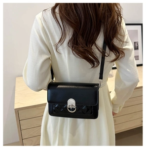 Detail of black quilted square shoulder bag with silver lock worn by model
