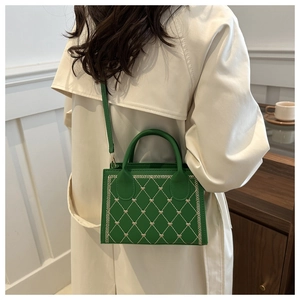 Close-up of green crossbody bag featuring beige diamond quilting and heart embroidery
