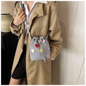 Dettaglio della borsa a secchiello grigia con toppe a cuore colorate su un cappotto kaki