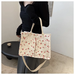Detail of canvas tote bag featuring red cherry prints and two functional front pockets