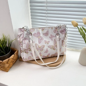 White tote bag with pink butterfly embroidery and silver chain straps on a wooden stand