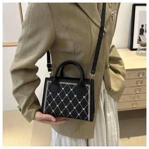 Detail of black crossbody bag with quilted heart embroidery and rounded handle