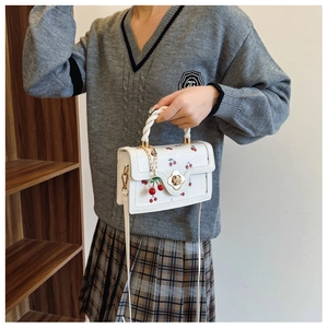 Detail of white cherry print handbag featuring gold floral twist lock and braided handle