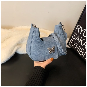 Détail du sac demi-lune bleu denim avec boucle papillon et poignée tressée