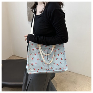 Detail of light blue canvas tote bag featuring red cherry prints and dual front pockets