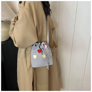 Dettaglio borsa a secchiello in denim grigio con patch a cuore colorati e trench kaki
