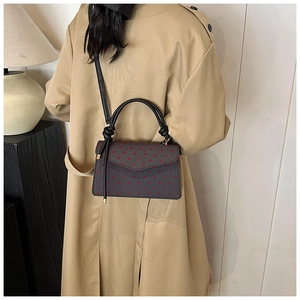 Lifestyle shot of a stylish black polka dot crossbody bag worn with a beige trench coat